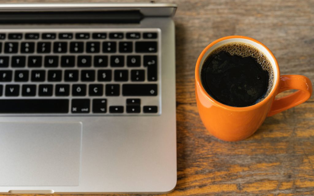a coffee alongside a macbook showing the importance of coffee in workplace wellness