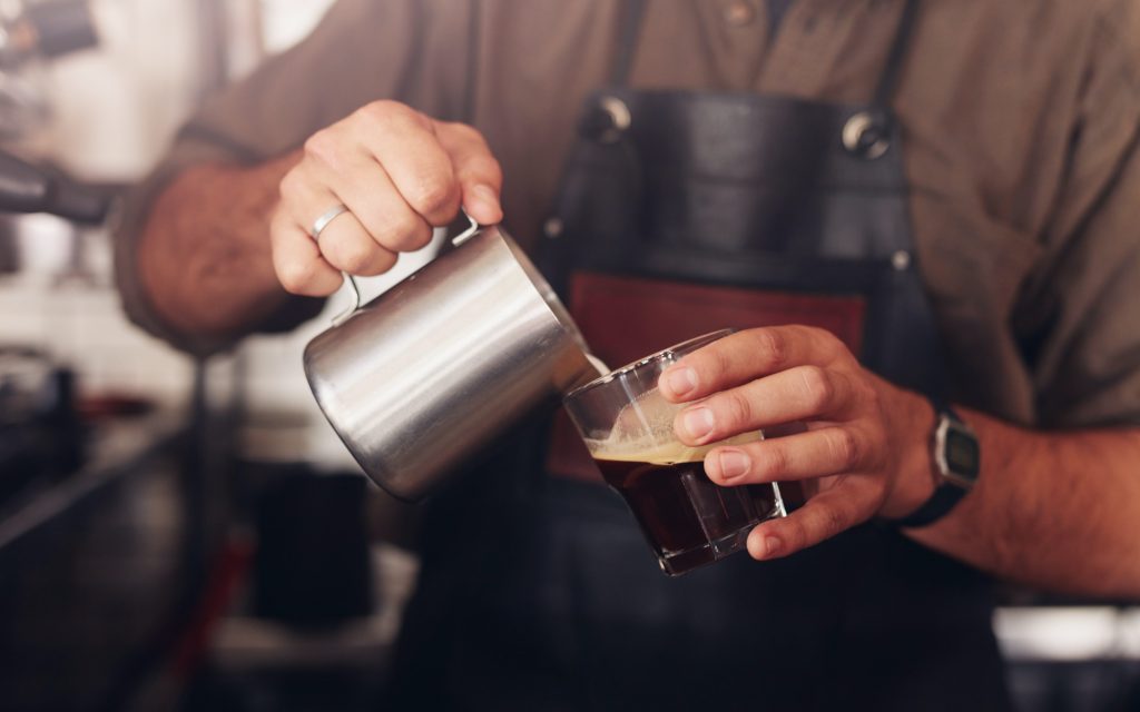 Cropped shot of barista pouring milk in to a cup of coffee.