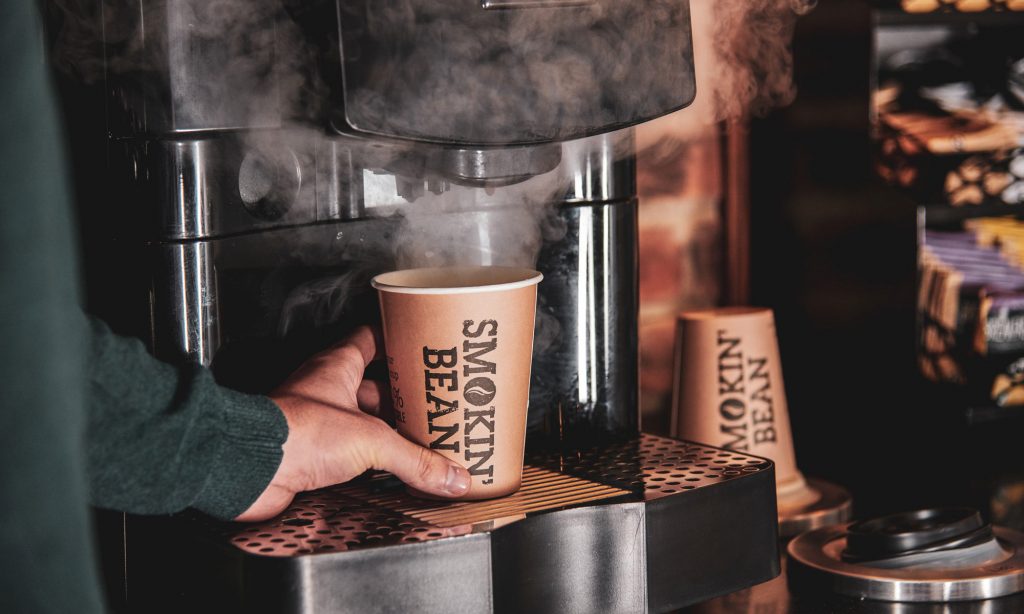 A Carimali superautomatic espresso machine pours coffee into a Smokin' Bean cup.